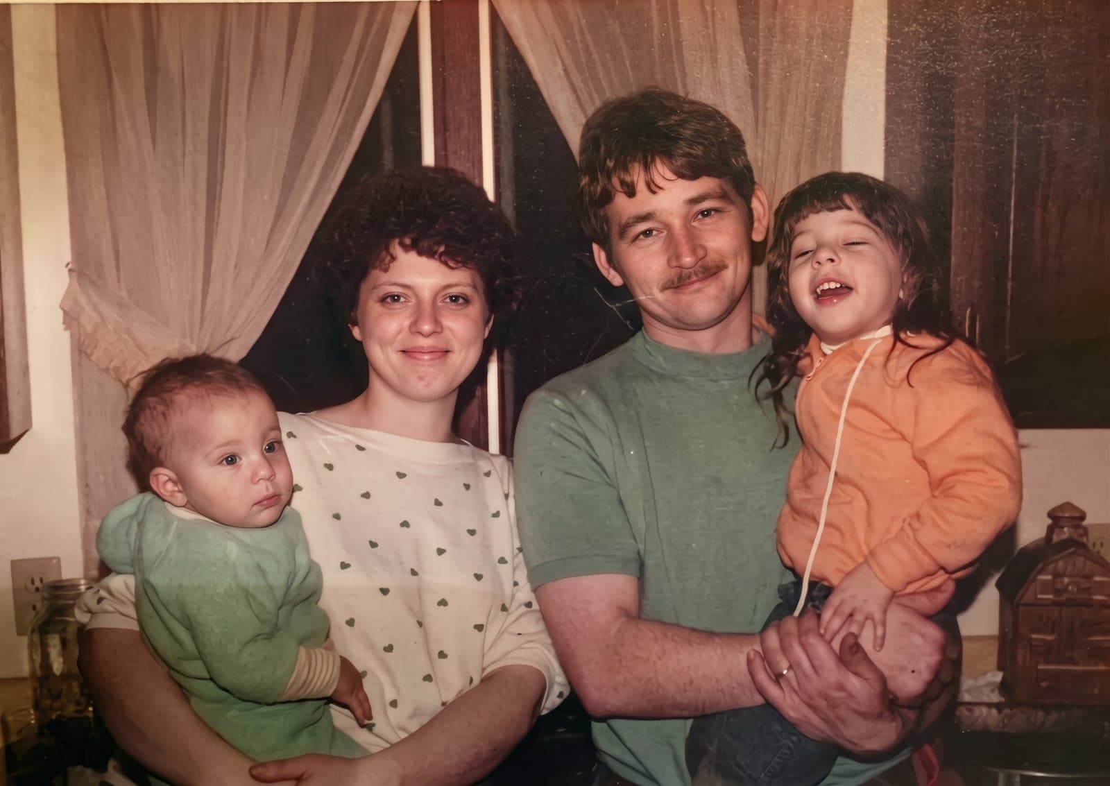 A faded 1980s photo of a couple holding a baby and a toddler, upscaled