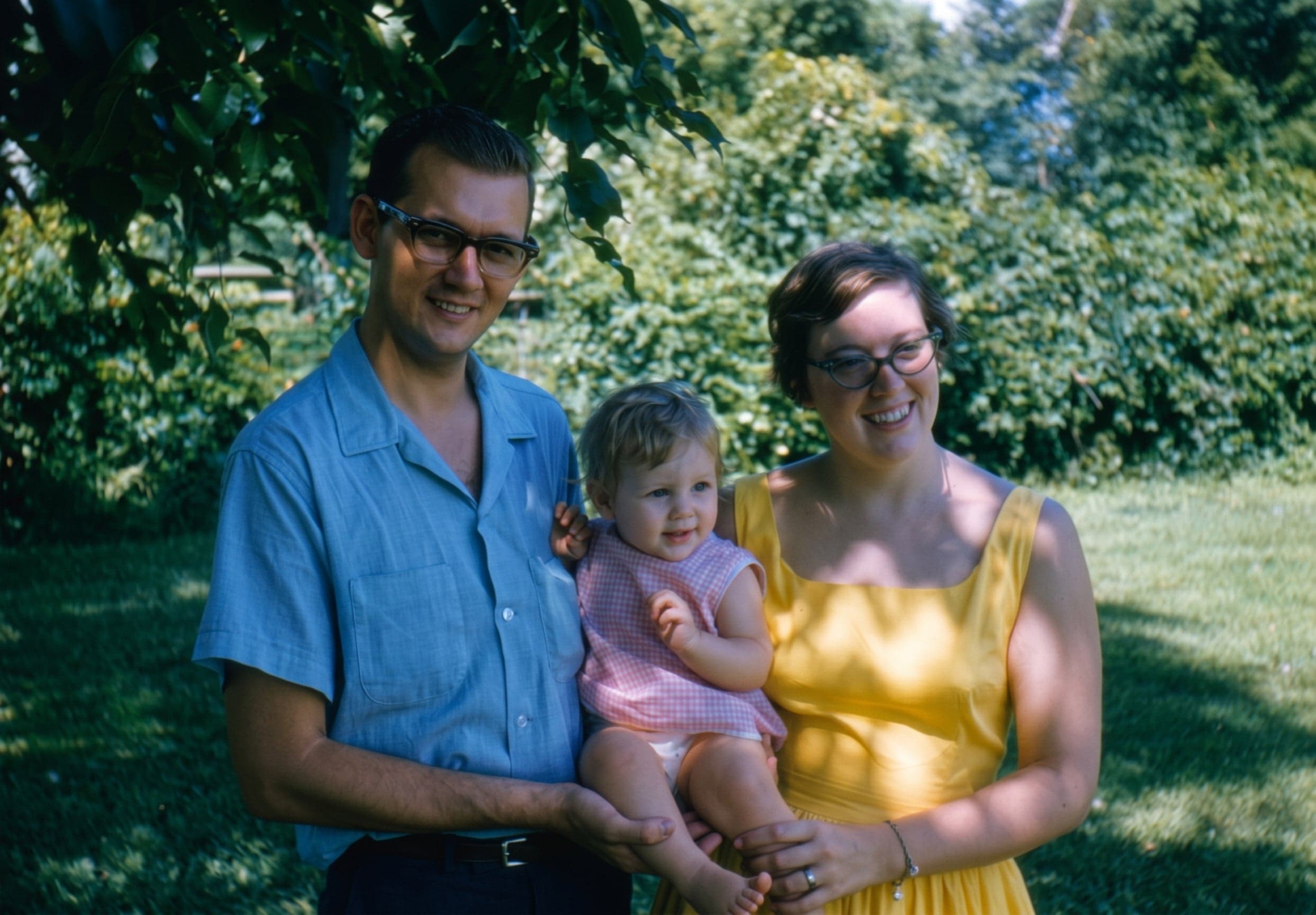 A 1960s colour slide of a couple holding a baby in a garden, upscaled