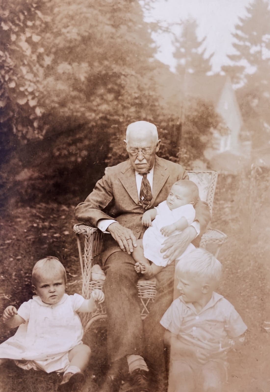 A creased sepia photo of an elderly man in a wicker chair with three small children, upscaled