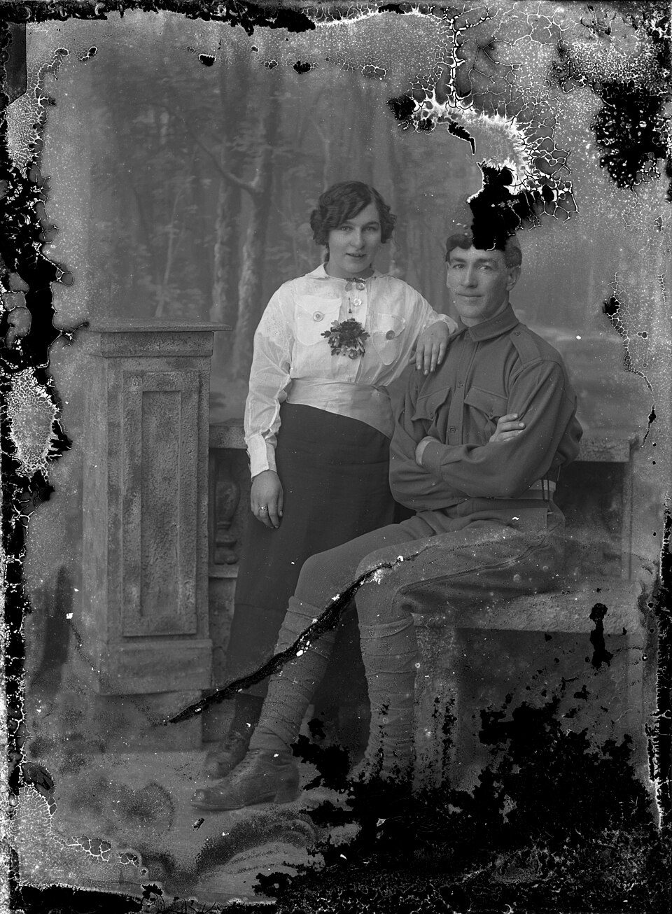 A soldier and a young woman posed by a stone bench, on a plate flaking at the edges, before restoration