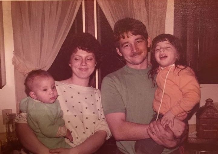 A faded 1980s photo of a couple holding a baby and a toddler, before upscaling