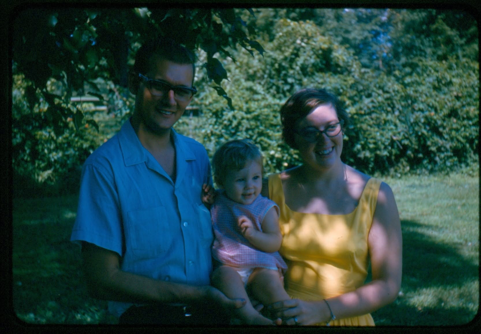 A 1960s colour slide of a couple holding a baby in a garden, before upscaling